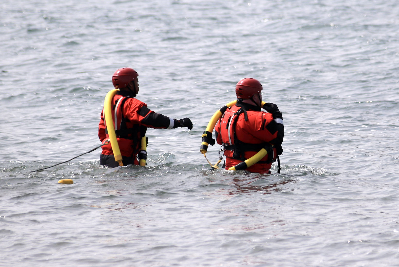 Two men in red wetsuits in the water with rescue ropes.
