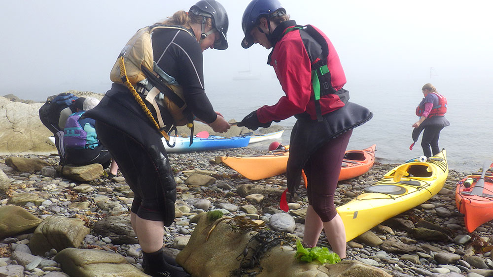 Group of kayakers on a rocky beach checking equipment