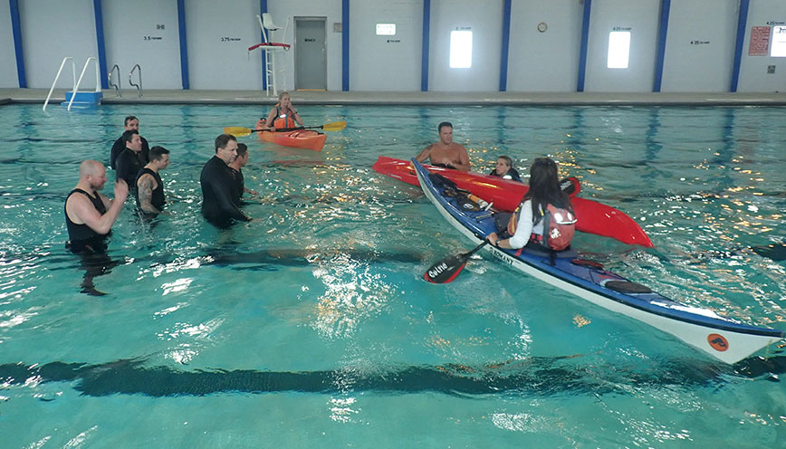 Group of kayakers in indoor pool with instructor